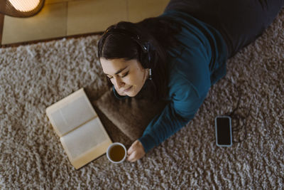 Woman with eyes closed enjoying listening to music while lying on carpet at home