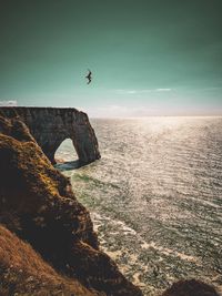 Man jumping on rock by sea against sky