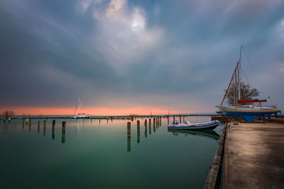 Sailboats moored at harbor against sky during sunset