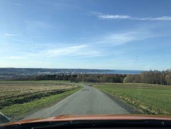 Road amidst field seen through car windshield