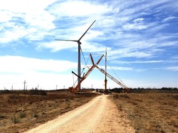 Windmill on field by road against sky