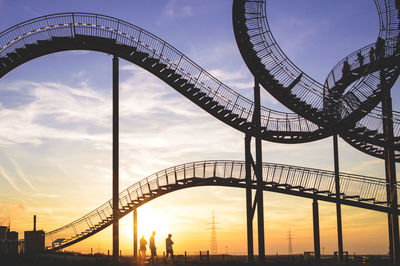 People in front of an architectural work of art  in front of the setting sun.