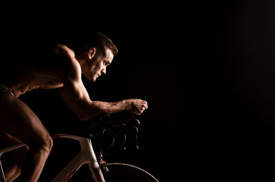 Side view of shirtless man cycling against black background