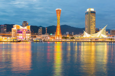 Illuminated buildings by river against sky at night