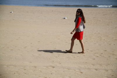 Side view of young woman walking at beach during sunny day