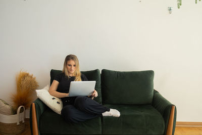 Woman working at home from couch with laptop on her lap. home office concept. gray notebook