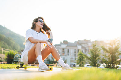 Slim young woman with long blonde hair in sports clothes with longboard in outdoor skatepark 