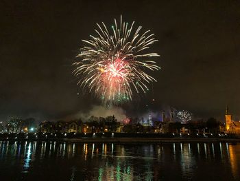 Firework display over illuminated city against sky at night