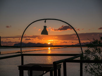 Silhouette railing by sea against sky during sunset