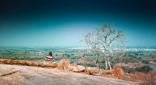 Friends sitting on land against clear blue sky