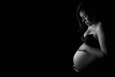 Side view of pregnant woman standing against black background