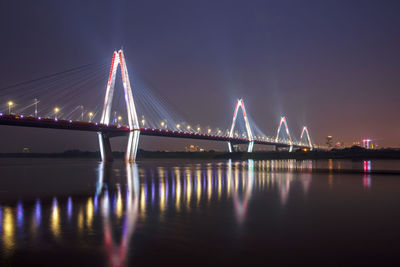 Illuminated bridge over river against sky at night