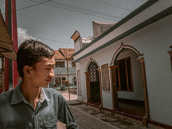 Young man looking away against buildings in city