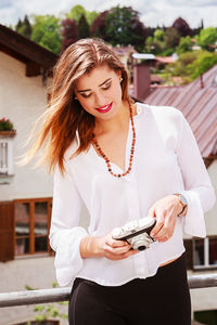 Young woman holding camera while standing outdoors