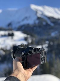 Cropped hand holding camera on snowcapped mountain