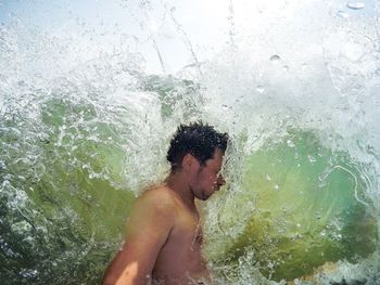 Side view of shirtless man amidst splashing wave in sea