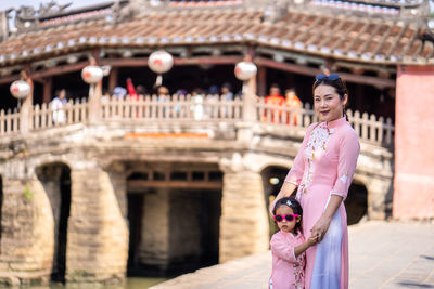 Portrait of mother and daughter standing against built structure