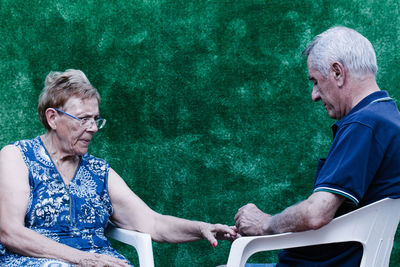 Old man painting his wife's nails red sitting on a plastic chair