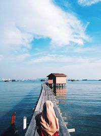 Rear view of woman standing on pier over sea against cloudy sky