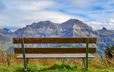 Empty bench on snowcapped mountains against sky
