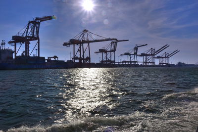 Silhouette cranes on pier by sea against sky