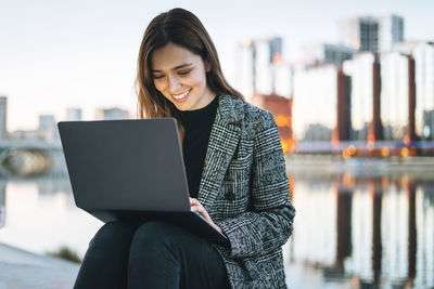 Young woman using laptop while sitting on railing