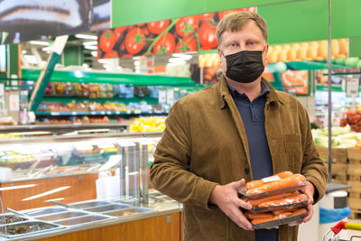 An adult tall man in a black protective mask in a grocery store with a package of carrots.