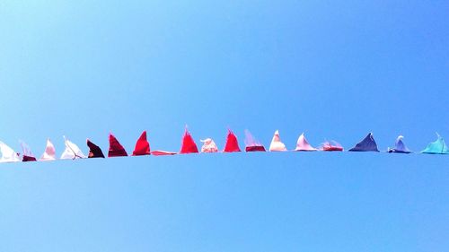 Low angle view of bunting flags hanging against clear blue sky