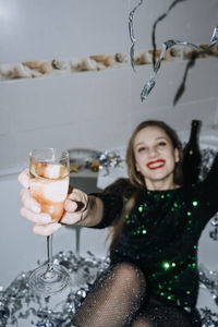 New years party celebration. happy young woman in evening dress sitting in the bathtub drinking