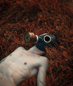 Shirtless man wearing gas mask while lying on grassy land