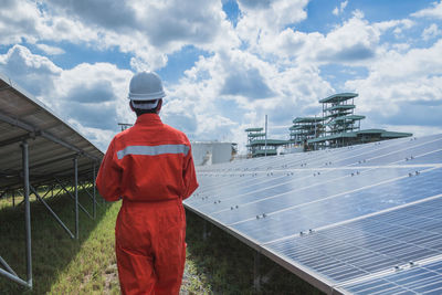 Rear view of worker wearing reflective clothing while standing on solar panel against sky