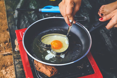 Cropped image of woman making heart shape fried egg on field