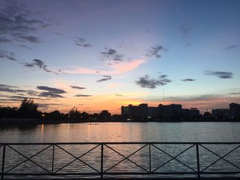 Silhouette city by river against sky during sunset