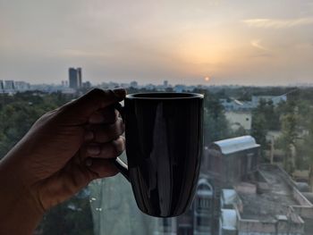 Midsection of man holding cityscape against sky during sunset