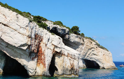 Rock formation by sea against clear blue sky