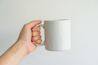 Cropped image of hand holding coffee cup against white background