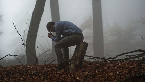 Side view of depressed man sitting on tree stump in forest during foggy weather