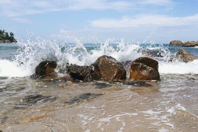 Sea waves splashing on rocks against sky