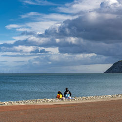 Couple sitting by sea against sky