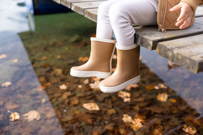 Toddler boy in brown robber boots sitting on the pear at mountain lake