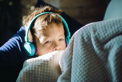Cute boy looking away while listening music under blanket at home