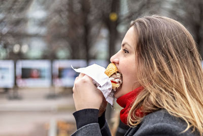 Young hungry woman eats burger and takes lunch break outdoors in park.fast food. takeaway food 