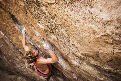 High angle view of shirtless hiker climbing rock