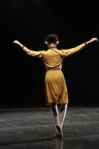 Rear view of full length of man dancing against black background