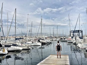 Rear view of man standing at harbor against sky