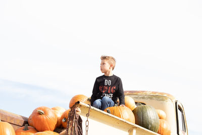 Low angel view of boy sitting on pumpkin in truck against sky