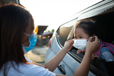 Close-up of mother wearing flu mask to girl in car