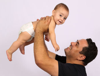 Smiling father picking up cute shirtless son while standing against colored background