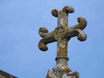 Low angle view of cross sculpture against clear blue sky