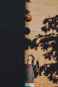 Male teenager wearing backpack playing with soccer ball against brick wall